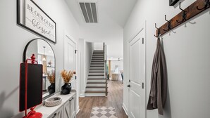 Un couloir avec un escalier, un miroir, un objet rouge posé sur un comptoir et un porte-manteau.