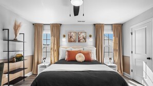 Une chambre à coucher comprenant un lit, des tables de chevet, une étagère avec des objets décoratifs et une vue sur l’extérieur.