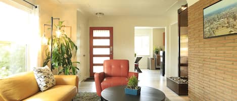 Un salon moderne avec un canapé jaune, un fauteuil rouge, une table basse ronde et une plante en pot.