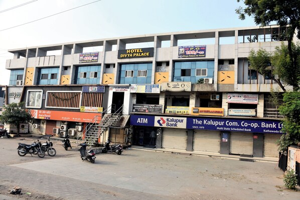 Um edifício de vários andares com uma placa indicando Hotel Divya Palace, um caixa eletrônico e o Banco Kalupur Com. Co-op.