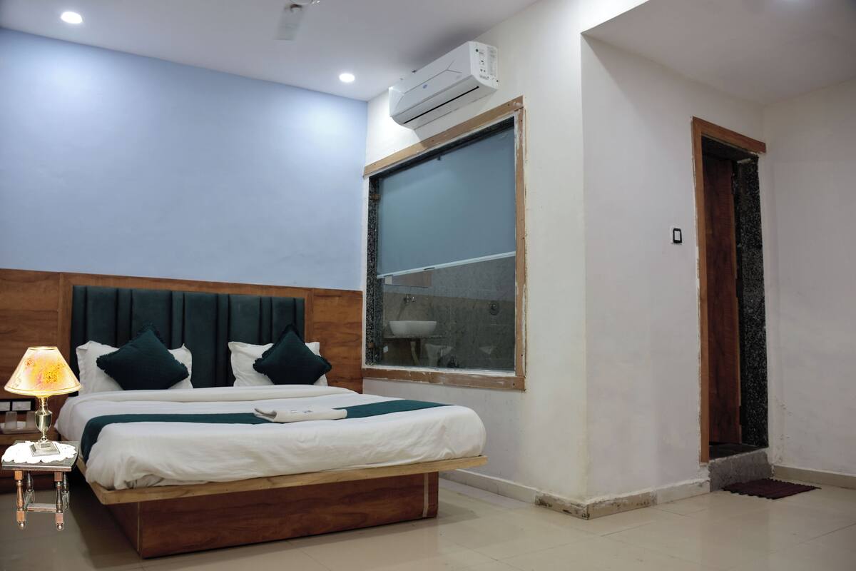 Un dormitorio con cama, mesita de noche, lámpara, aire acondicionado, ventana y puerta.