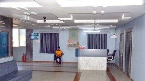 A reception area with a marble counter, a blue sofa, and a man sitting on a chair. - HOTEL DIVYA PALACE (Ahmedabad)