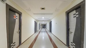 A long, narrow hallway with doors on both sides, a tiled floor, and a ceiling with recessed lighting. - HOTEL DIVYA PALACE (Ahmedabad)