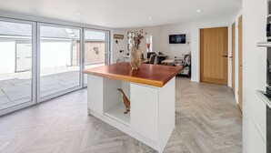Uma cozinha moderna com bancada de madeira, piso em padrão herringbone e uma porta de vidro deslizante para um pátio.