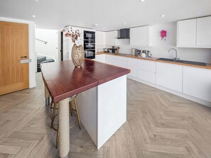 A modern kitchen with a wooden island, white cabinetry, and a herringbone-patterned floor. - 3 bedroom accommodation in Falmouth (Falmouth)
