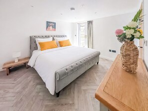 A bedroom with a bed, bedside table, bench, and a vase with flowers. - 3 bedroom accommodation in Falmouth (Falmouth)