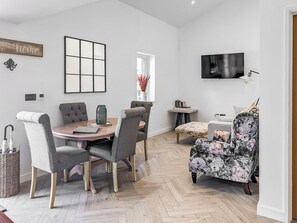 A modern living room with a dining area, a flat-screen TV mounted on the wall, and a floral armchair. - 3 bedroom accommodation in Falmouth (Falmouth)