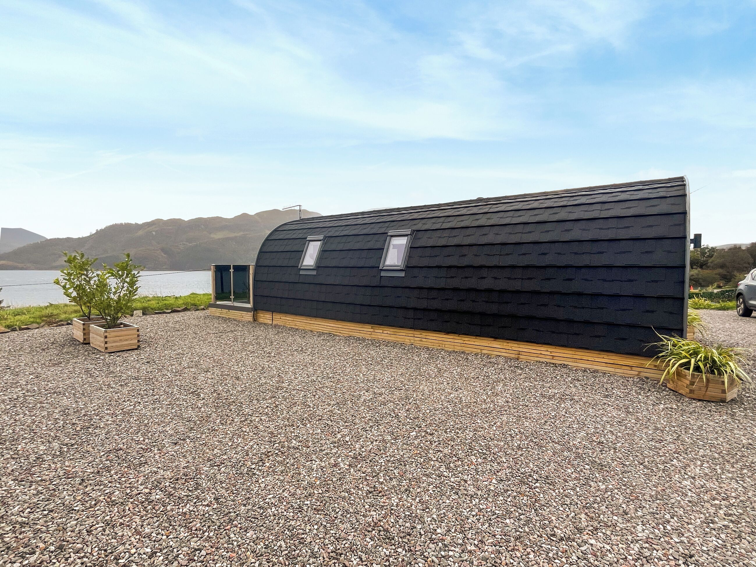 A modern, black, curved building with a wooden deck and two potted plants.
