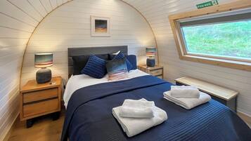 A cozy, curved room with a bed, nightstands, a window, and a fire exit sign.