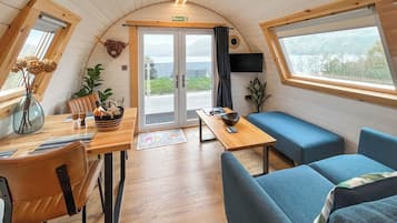 A cozy interior with a wooden table, blue seating, a TV, and a view through the door.