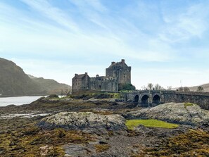 Eine historische Steinburg mit einer Brücke, umgeben von felsigem Gelände und einem Gewässer.