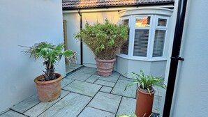 A narrow courtyard with tiled flooring, potted plants, a tiled roof, and a white building with shutters. - 2 bedroom accommodation in Peacehaven (Peacehaven)