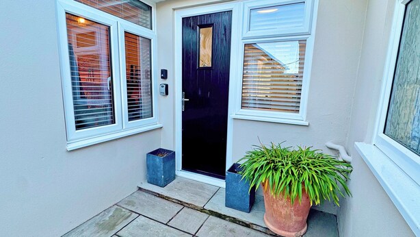 A house entrance with a black door, two windows with blinds, a potted plant, and a small blue planter. - 2 bedroom accommodation in Peacehaven (Peacehaven)