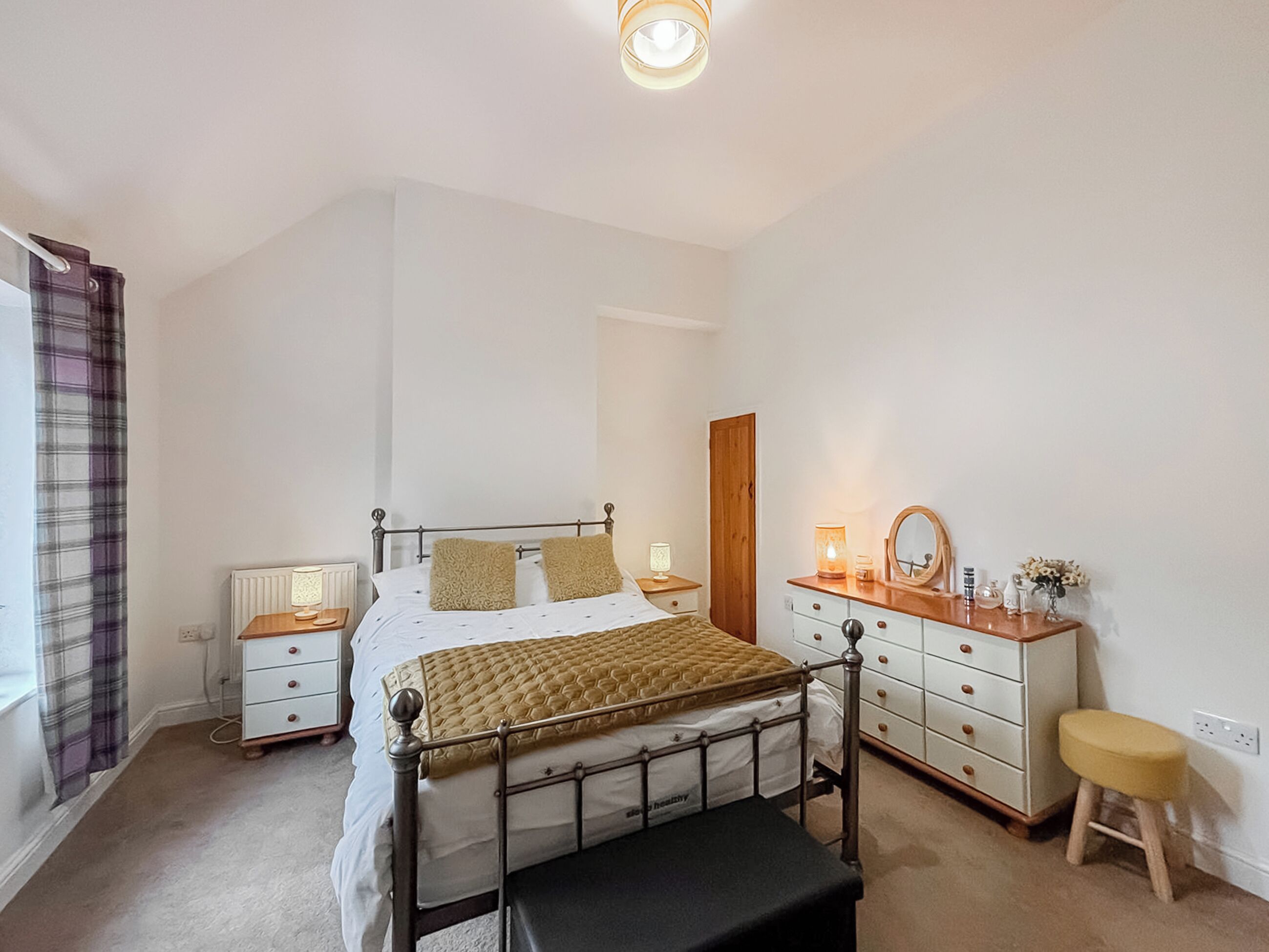 Un dormitorio con cama, mesitas de noche, cómoda, espejo y un taburete.