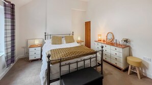 Une chambre à coucher comprenant un lit, des tables de chevet, une commode, un miroir et un tabouret.