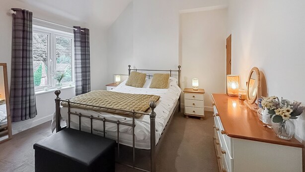 Une chambre à coucher avec un lit, des tables de chevet, une commode, un miroir et une fenêtre avec des rideaux.