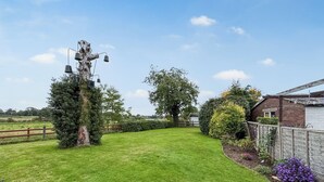 Une pelouse bien entretenue, une clôture en bois, un grand arbre et un petit abri de jardin.