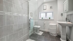 Une salle de bain moderne avec une douche à parois de verre, des toilettes, un lavabo et une fenêtre agrémentée de plantes.