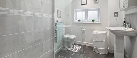 Un baño moderno con cabina de ducha de vidrio, inodoro, lavamanos y ventana con plantas.