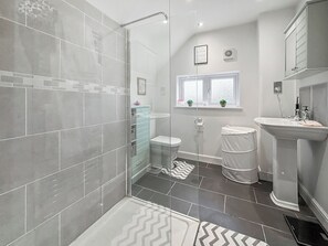 A modern bathroom with a glass shower enclosure, a toilet, a sink, and a window with plants. - 2 bedroom accommodation in Hinton, Market Drayton. (Hinton, Market Drayton.)