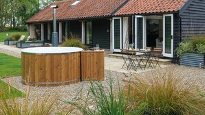 Une maison avec un toit en pente, un jacuzzi et une terrasse aménagée avec du mobilier d’extérieur.