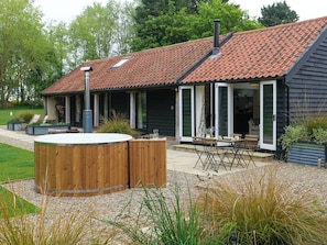 Een huis met een schuin dak, een bubbelbad en een terras met tuinmeubilair.