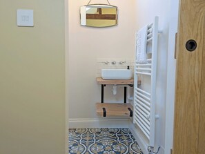 Un baño con lavamanos blanco, tocador de madera, baldosas de suelo estampadas, un espejo y un perchero para toallas.