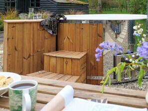Un espace extérieur aménagé avec des meubles en bois, comprenant un banc, une table avec une tasse et une assiette, et un petit radiateur.