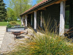 Una cabaña de madera con porche cubierto, un hogar y un jardín con pastos altos.