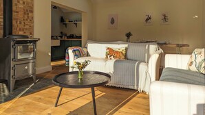 Un salon chaleureux avec une cheminée, une table ronde ornée d’un vase et un canapé agrémenté d’un coussin à motifs équestres.