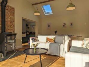 Una sala de estar acogedora con chimenea, una mesa redonda con un florero y un sofá con un cojín de caballos.