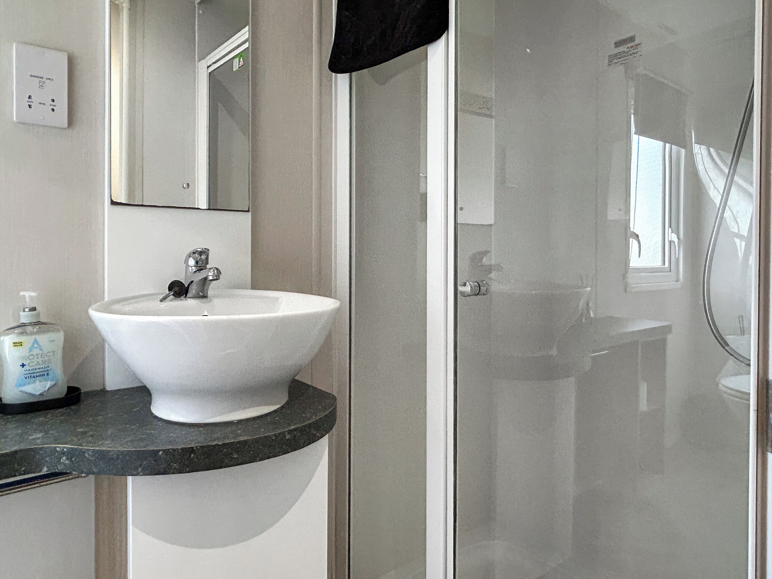 Een badkamer met een wit wastafelmeubel, een spiegel en een douchecabine van glas.