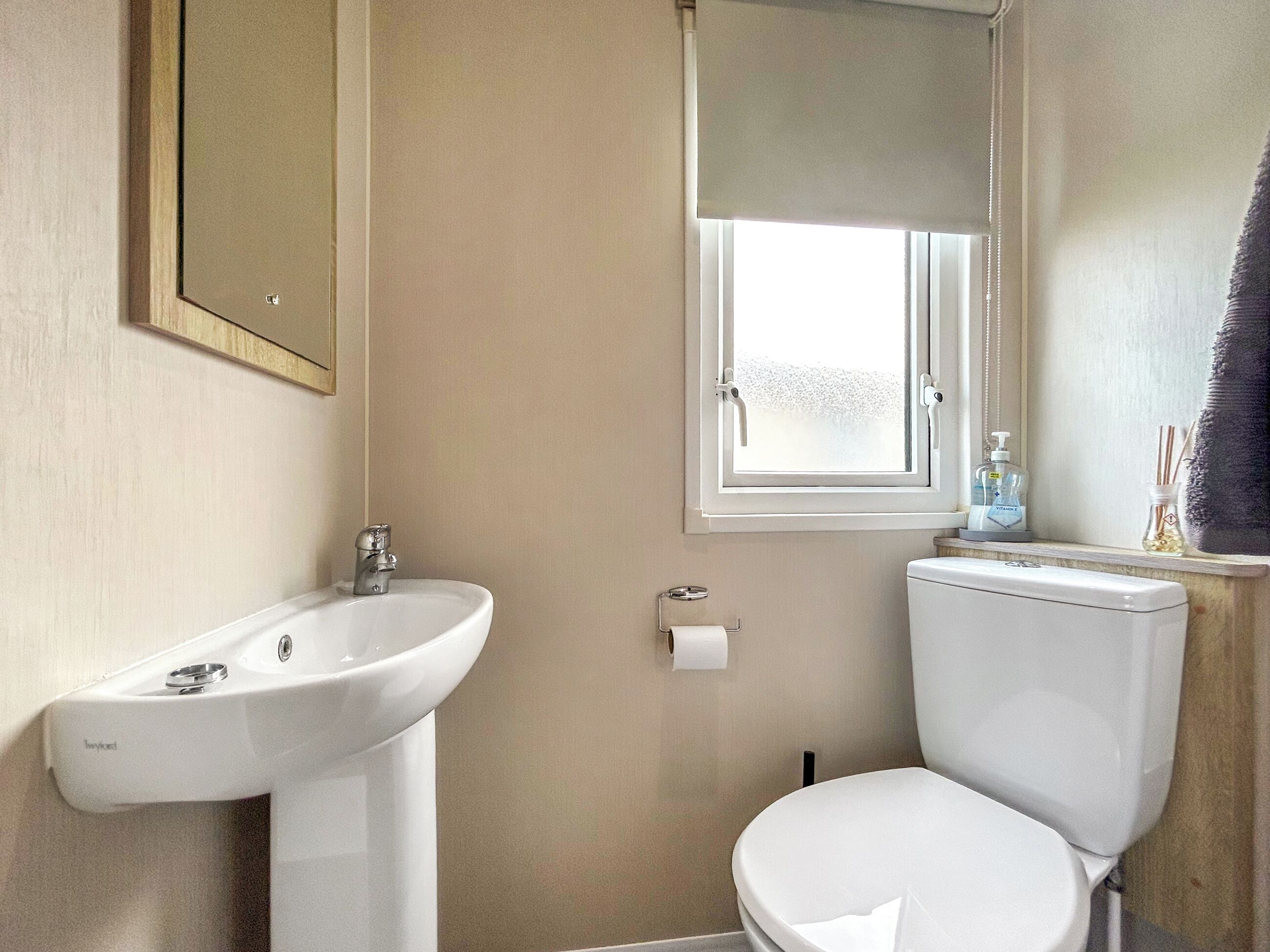 A bathroom with a white sink, toilet, and a window above the toilet.