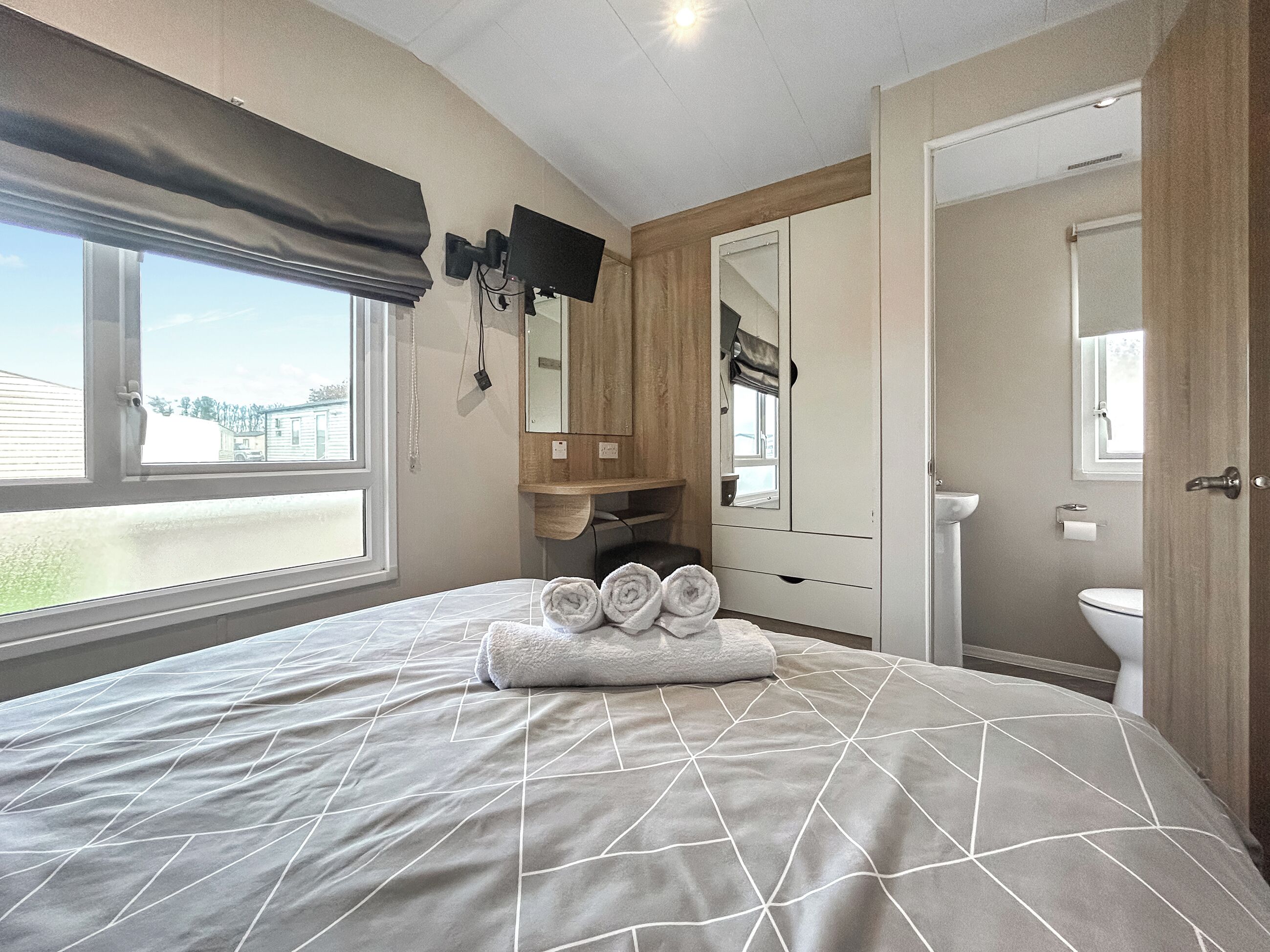 A bedroom with a bed, a TV mounted on the wall, a window, and a view of the outside.