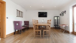 A dining area with a wooden table and chairs, a television mounted on the wall, and a cabinet with glass doors. - 6 bedroom accommodation in Llandevaud (Llandevaud)