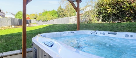 A hot tub under a wooden pergola in a backyard.