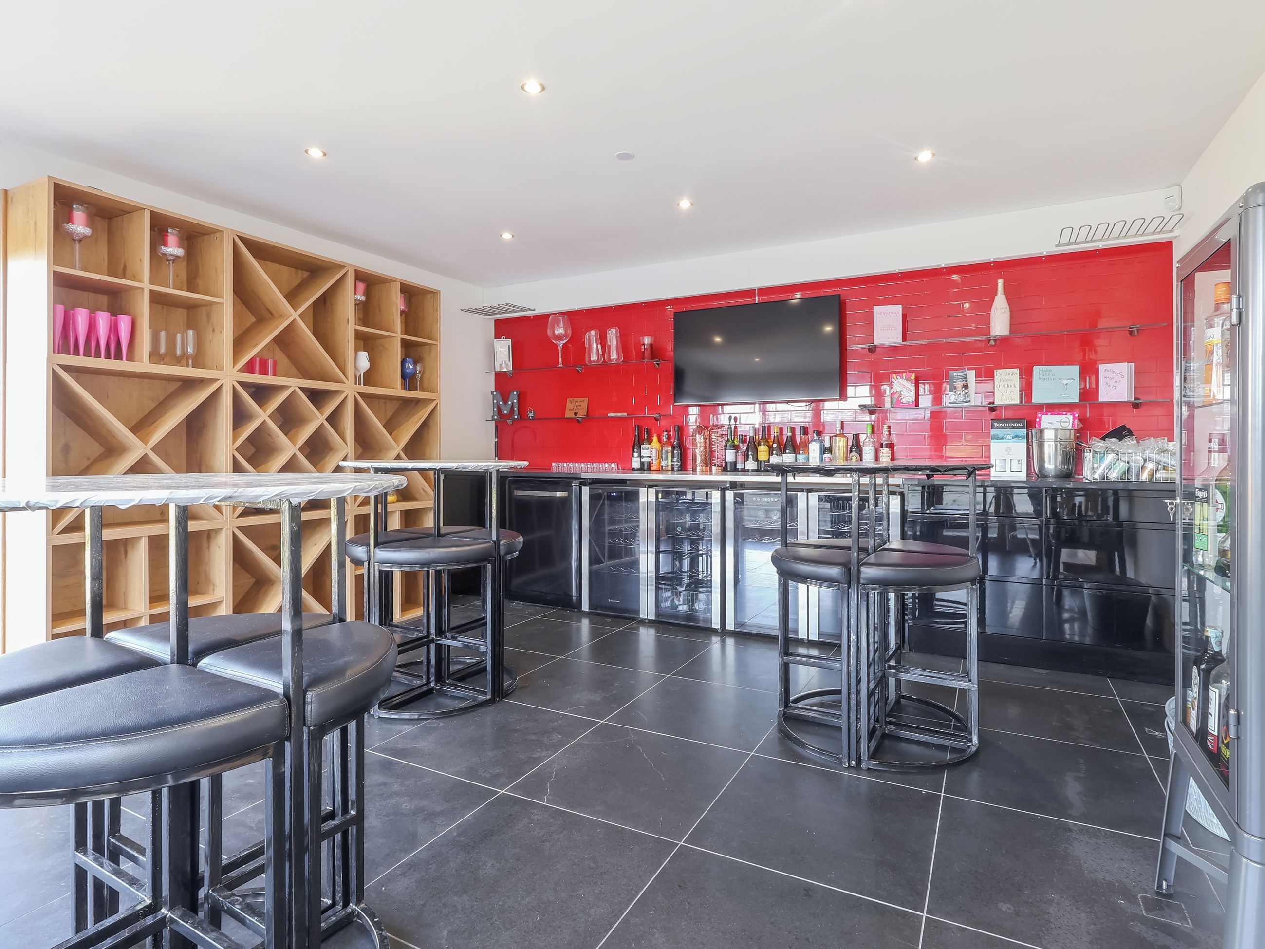 A bar area with stools, a TV mounted on the wall, and shelves with bottles.