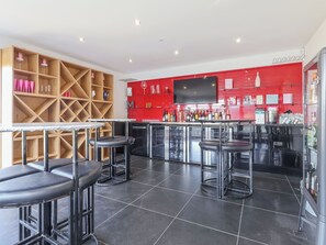 A bar area with stools, a TV mounted on the wall, and shelves with bottles.