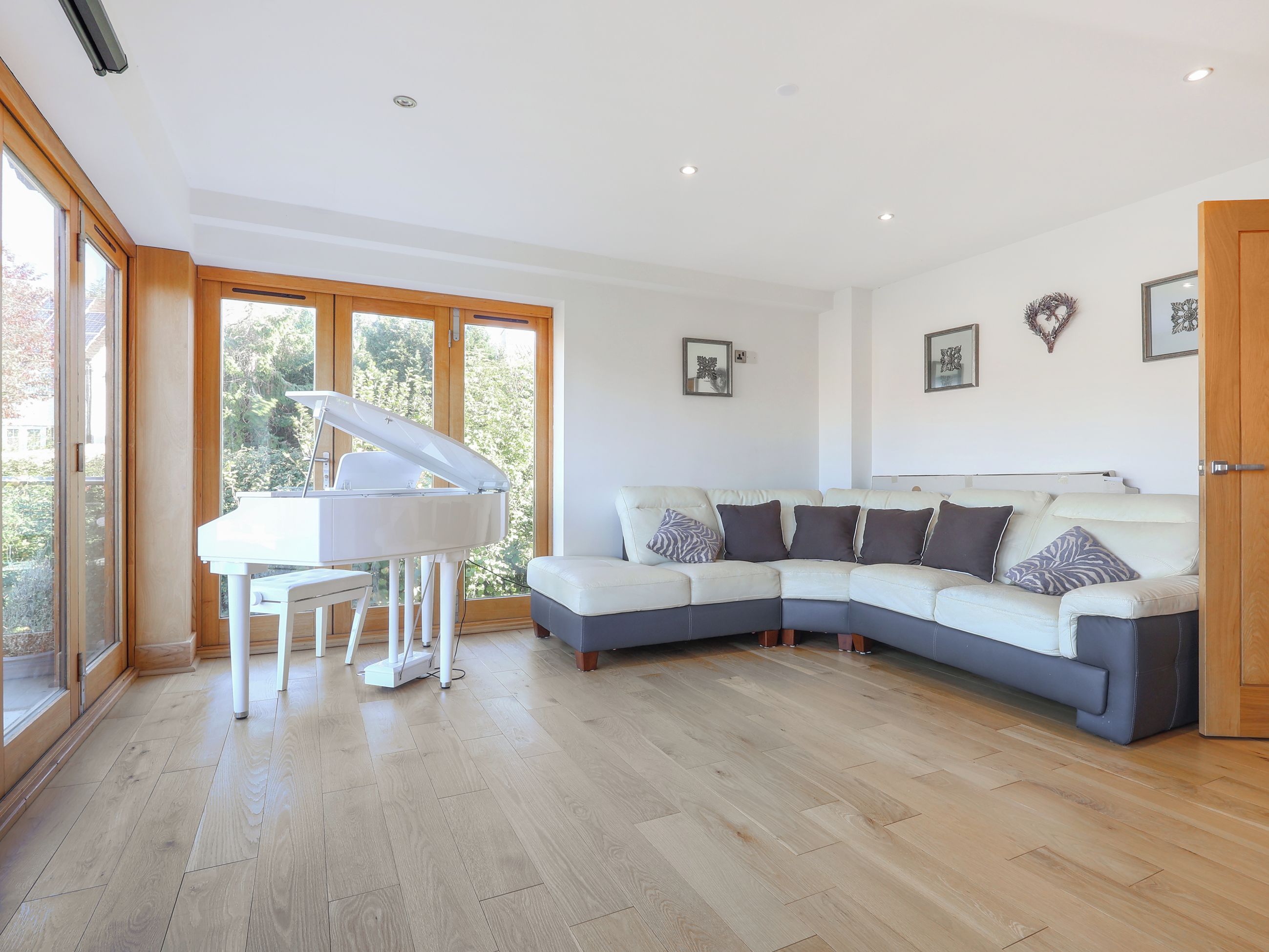 A modern living room with a sectional sofa, a grand piano, and large windows.