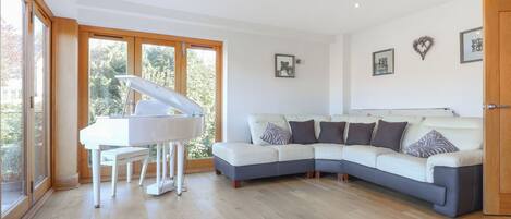 A modern living room with a sectional sofa, a grand piano, and large windows.