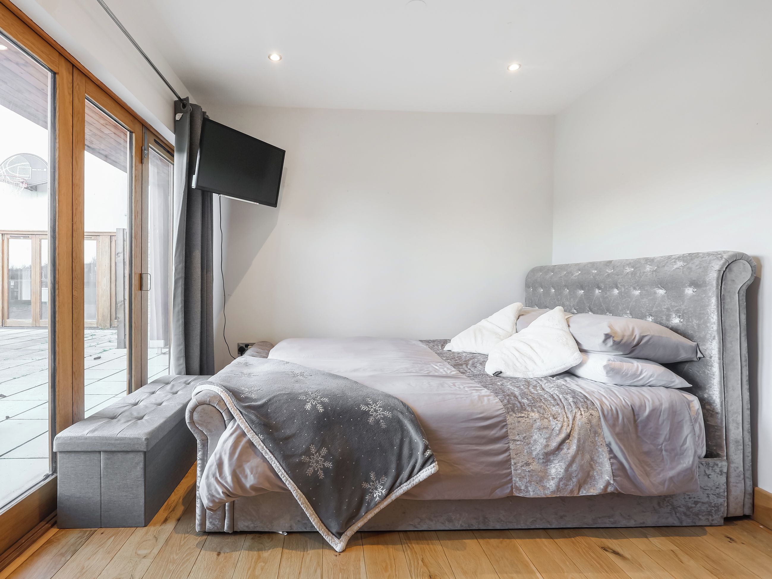 A bedroom with a bed, a TV, a bench, and a view of the outside.