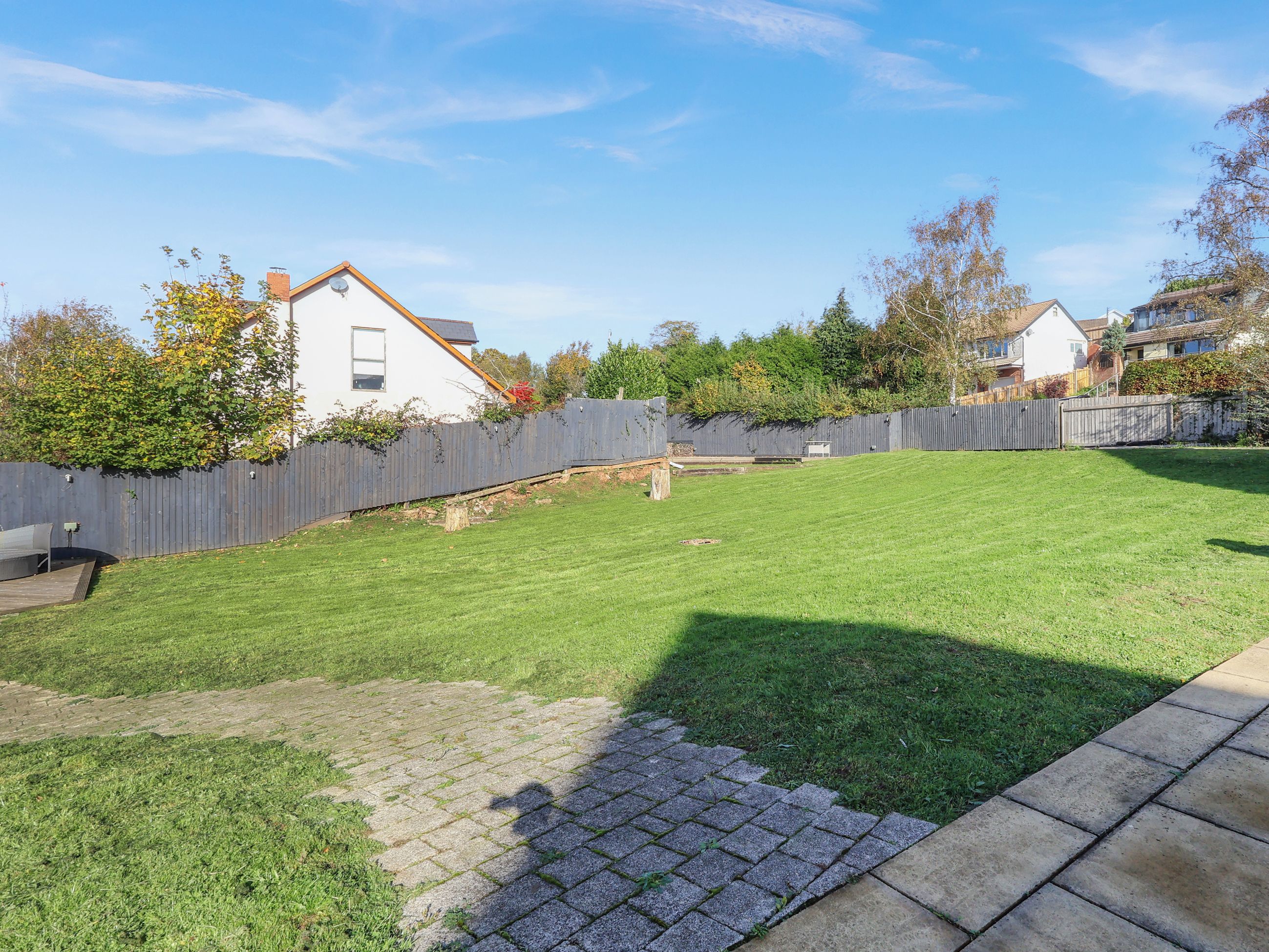 Un jardin avec une clôture en bois, une pelouse et un chemin pavé de briques.