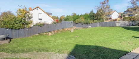 A backyard with a wooden fence, a lawn, and a brick pathway.