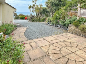 A stone pathway leading to a house with a garden, a wooden fence, and a red object in the background.