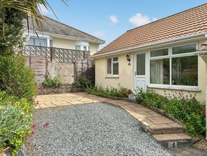 A residential property with a paved driveway, a gravel area, a wooden fence, and a house with a tiled roof and a white door.