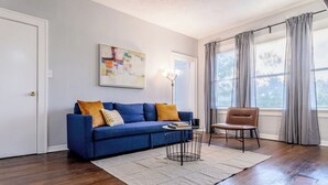 A living room with a blue sofa, a brown chair, a coffee table, and a painting on the wall. - The Montrose City-Chic Den, Near Medical Center (Houston)