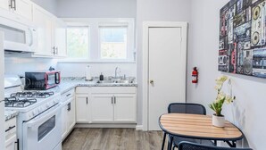 A compact kitchen with white cabinets, a microwave, a stove, and a sink. There's a small dining table with chairs and a potted plant. - The Montrose City-Chic Den, Near Medical Center (Houston)