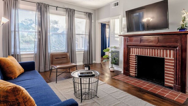 A living room with a blue sofa, a fireplace, a TV, and a window with curtains. - The Montrose City-Chic Den, Near Medical Center (Houston)