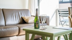 Et grønt bord med en vinflaske og to glas, placeret i en stue med en lædersofa og et vindue i baggrunden.