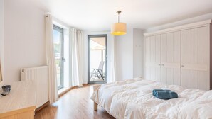 Et soveværelse med seng, skrivebord, radiator, vindue og dør til et udendørs område.